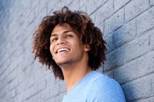 A man leans against a brick wall smiling because he got help from drug addiction treatment services